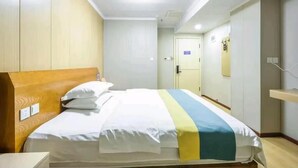 A hotel room with a wooden headboard, a bed with a white and blue striped bedspread, a bedside table, and a mirror on the wall. - Qiqiaowu Hotel Xinfadi Subway Station (Beijing)