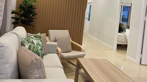Ett modernt vardagsrum med en soffa, fåtölj och soffbord, en väggpanel i trä och en takfläkt.
