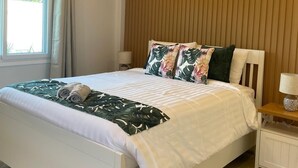 Een slaapkamer met een bed, een raam met gordijnen, een houten wandpaneel, een nachtkastje met lamp en een plafondventilator.