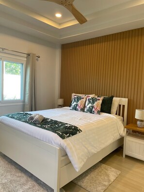 A bedroom with a bed, a window with curtains, a wooden wall panel, a bedside table with a lamp, and a ceiling fan. - Completely Private Pool Villa in Choeng Mon (Choeng Mon, Bophut, Koh Samui)