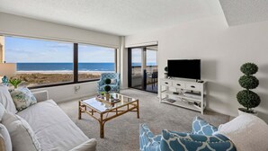 Un salon avec vue sur l’océan, un téléviseur et un meuble blanc.