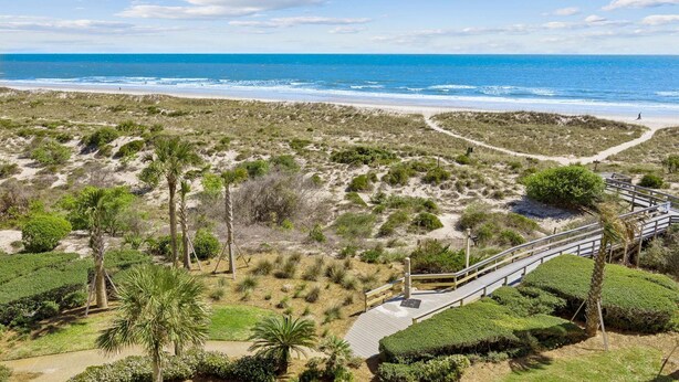 Un paysage côtier comprenant une plage, des dunes et une promenade en bois menant à la rive.