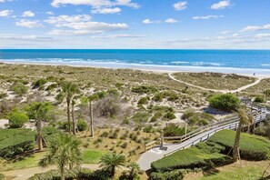 A coastal landscape with a beach, dunes, and a wooden boardwalk leading to the shore. - Classy Beachy-Vibe Oceanfront Condo-Walk to Beach (Fernandina Beach)