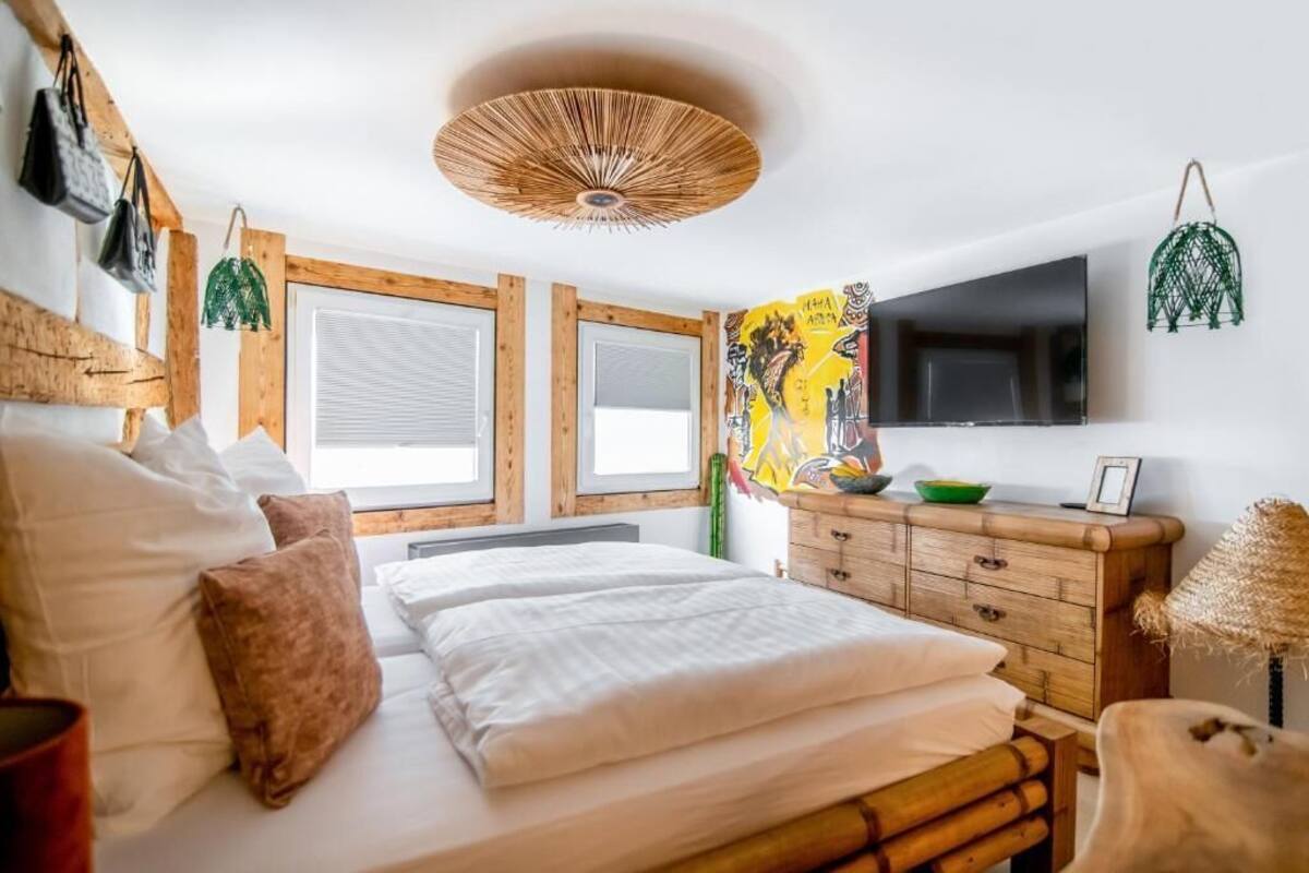 A bedroom with a bed, wooden headboard, a TV, a wall-mounted artwork, and a wooden dresser.