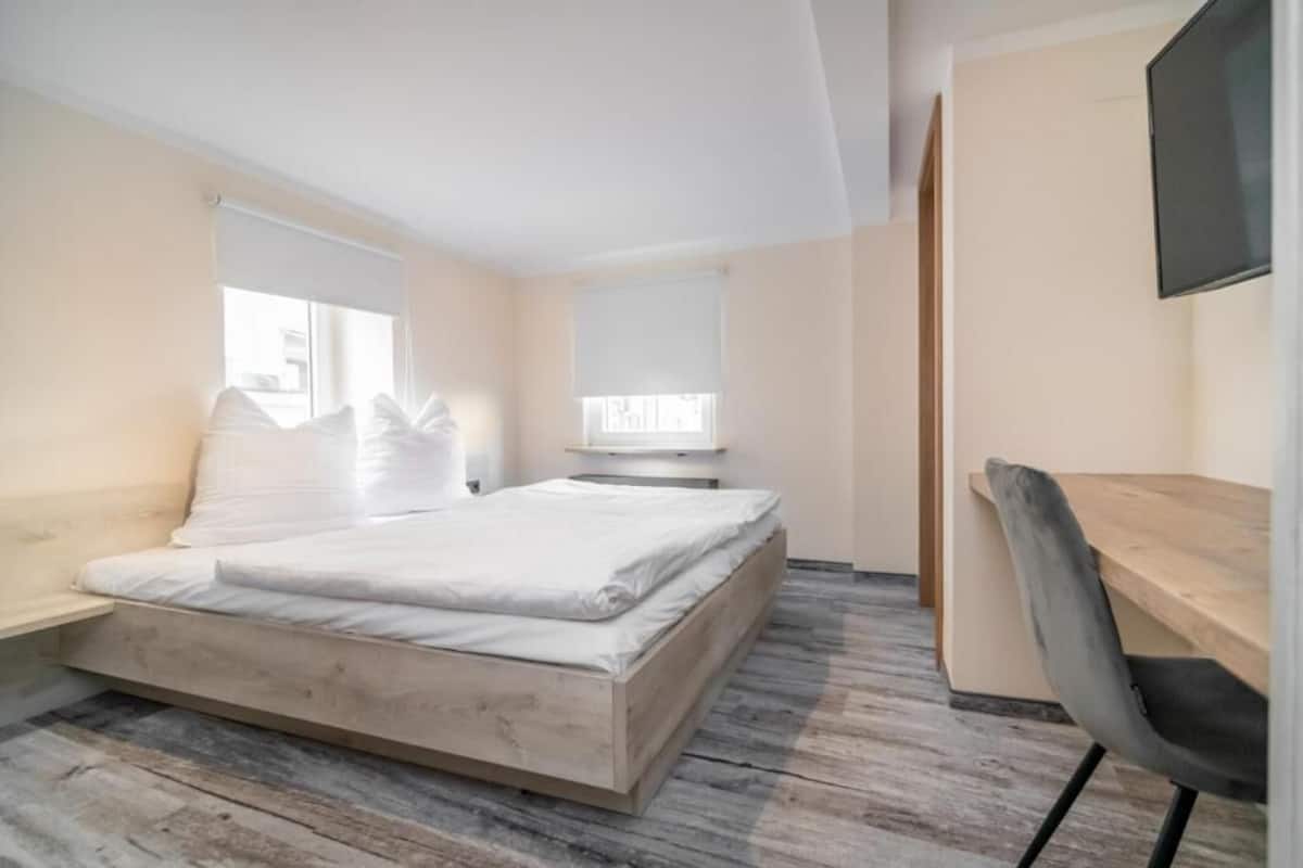 A bedroom with a bed, a desk, a chair, and a TV mounted on the wall.