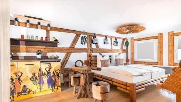 A room with a bed, wooden beams, a table, and a shelf with decorative items. - H M Boarding Houses (Lauf an der Pegnitz)