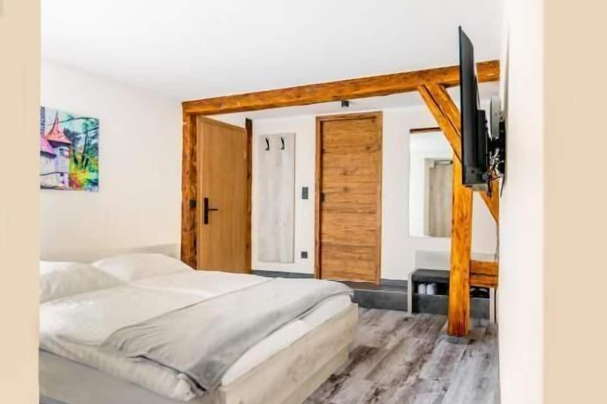 A bedroom with a bed, wooden beams, a TV, and a door.