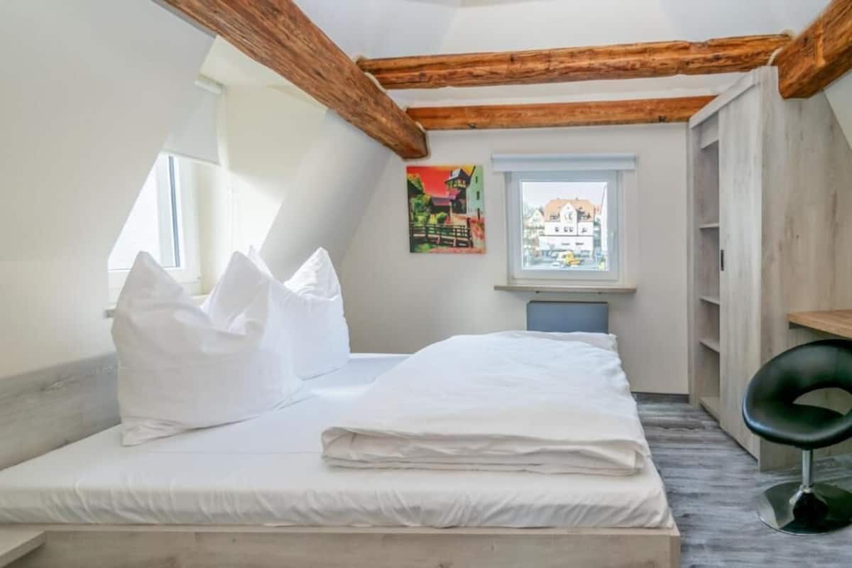 A bedroom with a bed, pillows, a window, a painting, and a desk.
