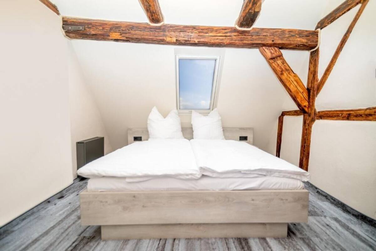 A bedroom with a wooden ceiling, a window, a bed, and a radiator.
