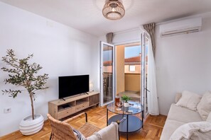 A modern living room with a flat-screen TV, a wooden TV stand, a wicker chair, a glass coffee table, and a potted plant. - Apt Xenia Walk To Beach /w Balcony, Medulin, Croatia (Medulin)