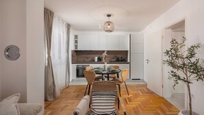 A modern kitchen with white cabinets, a dining area with wicker chairs, and a wooden herringbone floor. - Apt Xenia Walk To Beach /w Balcony, Medulin, Croatia (Medulin)