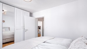 A minimalist bedroom with a large bed, a wardrobe, and a door leading to a bathroom. - Apt Xenia Walk To Beach /w Balcony, Medulin, Croatia (Medulin)