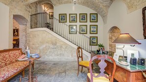 A stone-walled room with a staircase, a sofa, a desk with a lamp, and framed pictures on the wall. - Borgo Hedone - Boutique Blu, Scicli, Italy (Scicli)