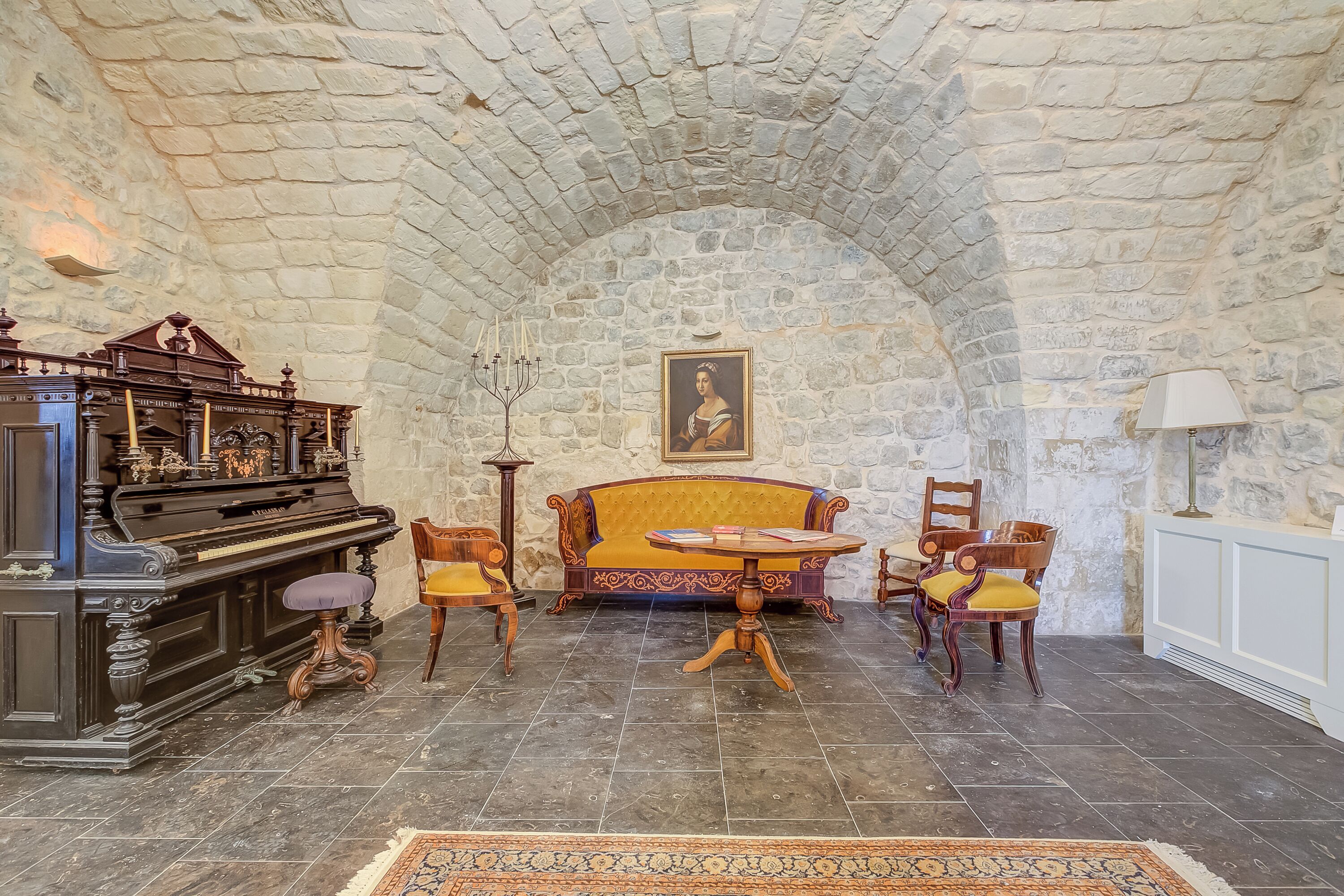 A room with a stone ceiling, a piano, a sofa, and a table with chairs.