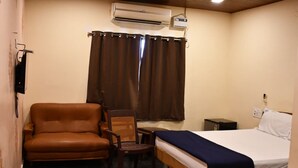 Une chambre à coucher comprenant un lit, une chaise, une petite table, un climatiseur et une fenêtre avec des rideaux.