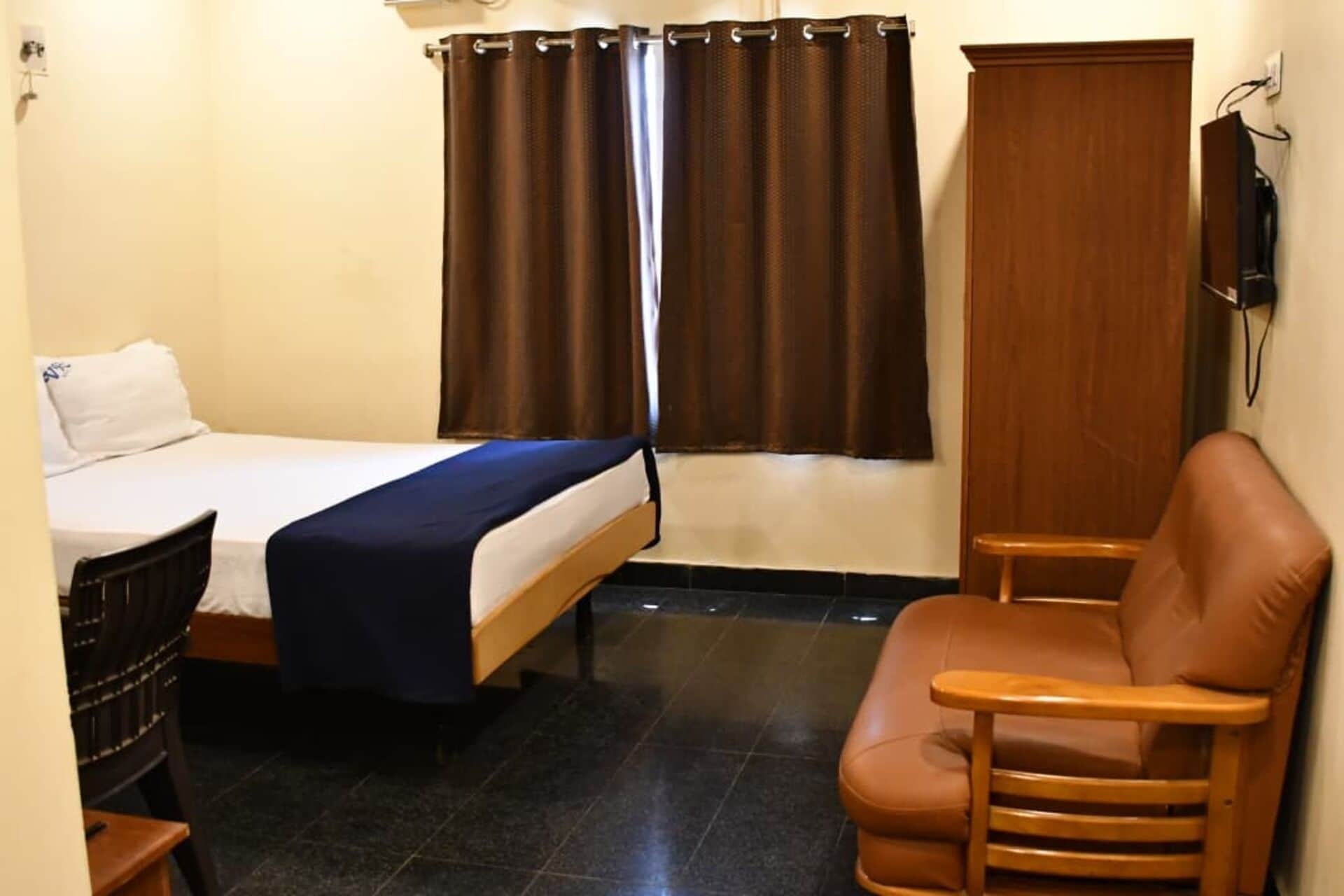 Une chambre d’hôtel avec un lit, une chaise, une télévision et une fenêtre avec des rideaux.