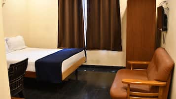 Une chambre d’hôtel avec un lit, une chaise, une télévision et une fenêtre avec des rideaux.