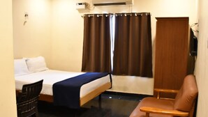 Une chambre d’hôtel avec un lit, une chaise, un bureau et une fenêtre avec des rideaux.