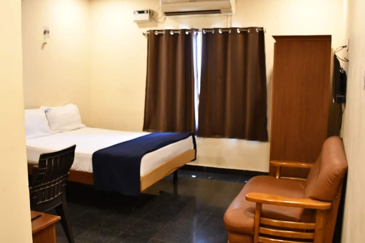 A hotel room with a bed, a chair, a desk, and a window with curtains.