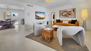 Ein modernes Wohnzimmer mit Flachbildfernseher, einer Couch, einem Couchtisch und einem Essbereich mit Stühlen.