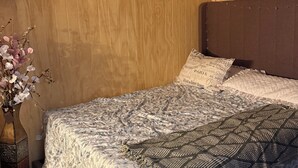 Ein Schlafzimmer mit einem hölzernen Kopfteil, einer zudeckenden Bettdecke mit Blumenmuster, einer Zier-Vase mit Blumen und einer dekorativen Zudecke.