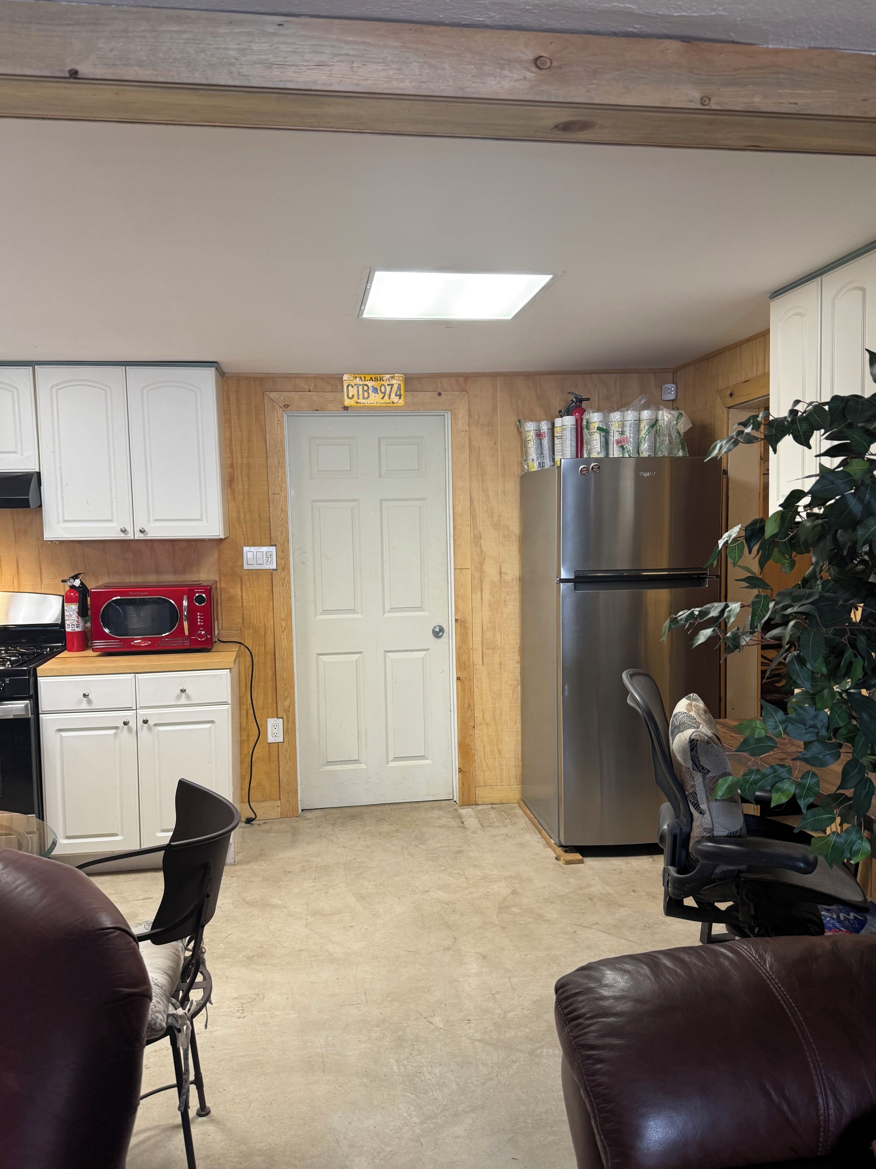 Una cocina con armarios de madera, microondas, refrigerador y una puerta con una placa de matrícula.