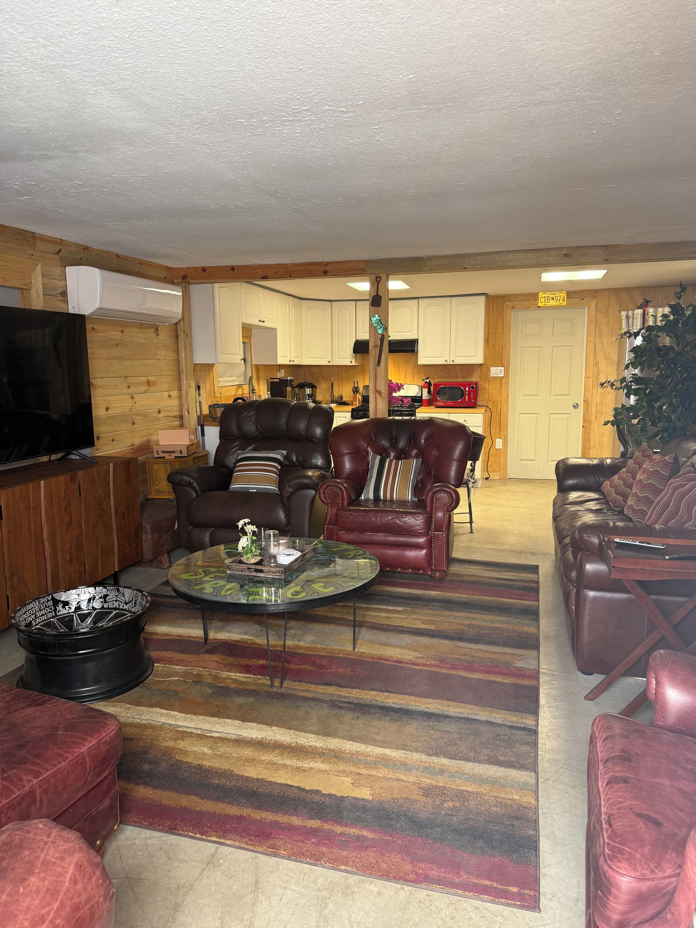 Sala de estar con sofás de cuero, una mesa de centro, un televisor y una cocina al fondo.