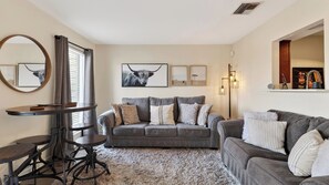 A living room with a grey sofa, a round table, and a mirror. - Riverfront Rhythm by Avantstay Shared Pool + Balcony + River Views Walk to Broadway + Germantown (Nashville)