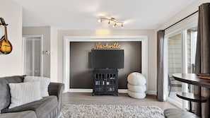 A living room with a TV, a guitar, a couch, and a fireplace.