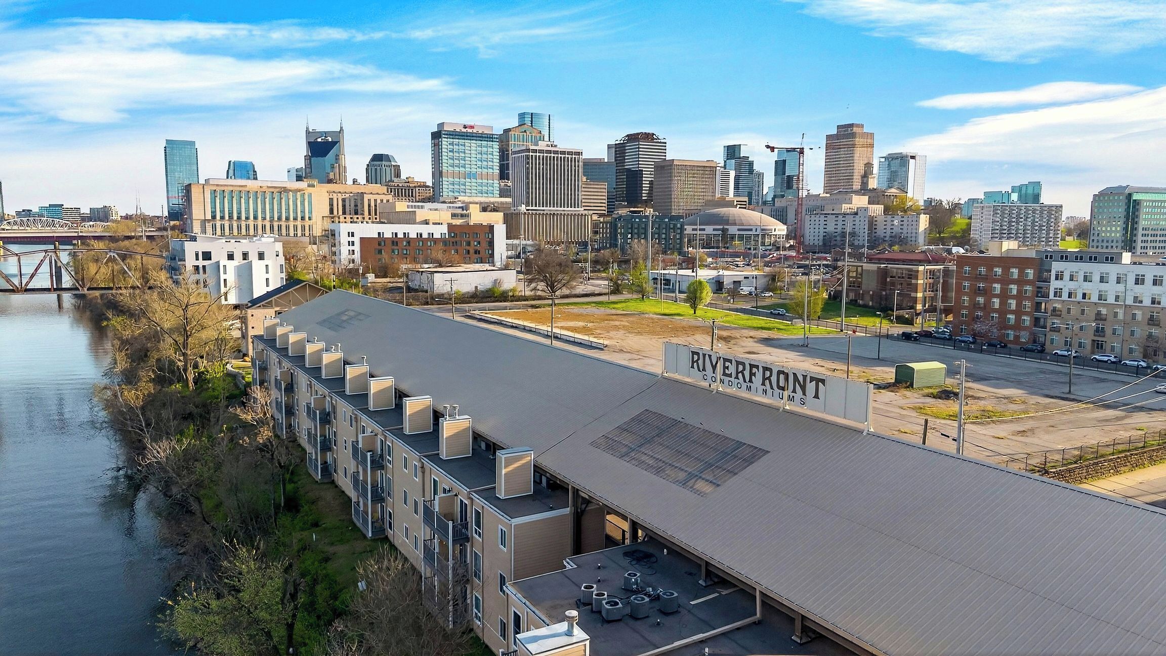 Un edificio moderno con tetto piatto, un cartello con la scritta 'Riverfront Condominiums' e vista sullo skyline cittadino con diversi edifici.