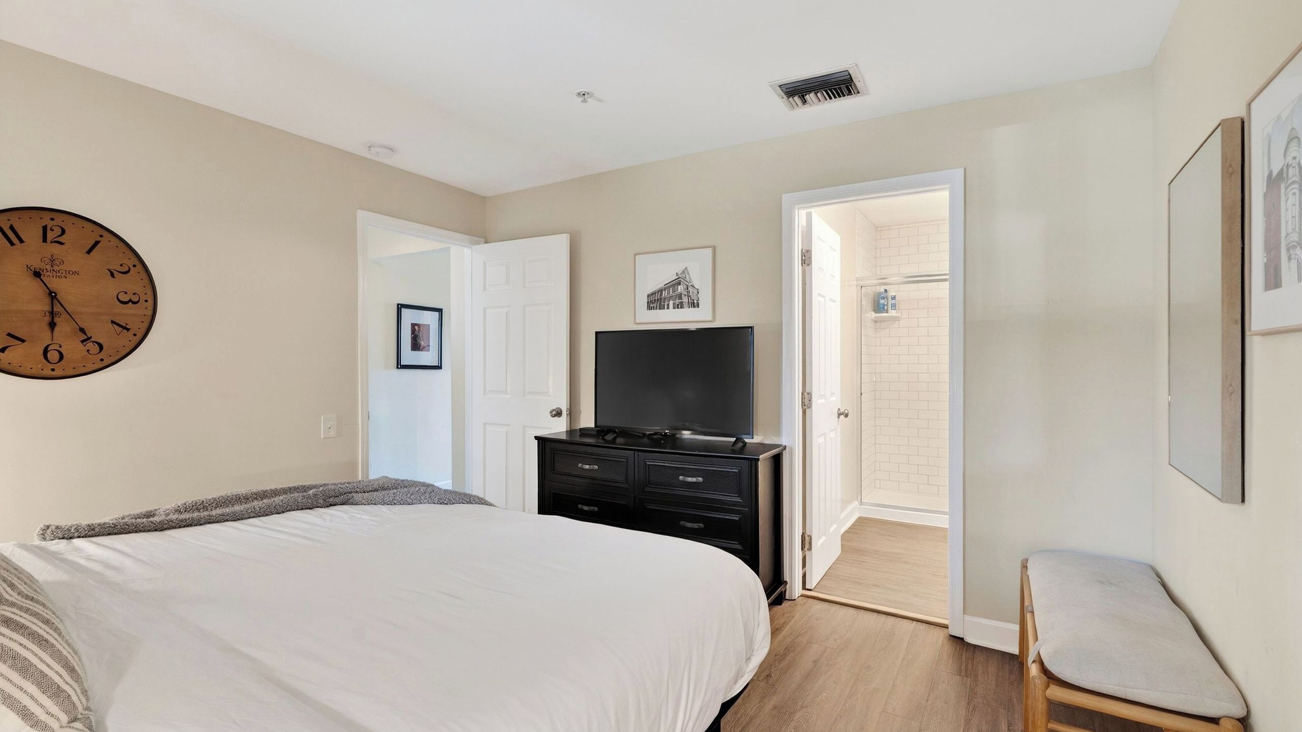 A bedroom with a bed, a dresser, a television, a framed picture, and a door leading to a bathroom.
