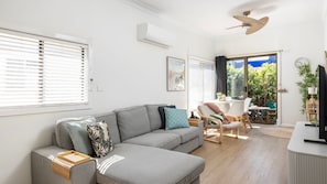 Una sala de estar moderna con un sofá gris, una mesita de madera, un ventilador de techo y vistas al exterior.