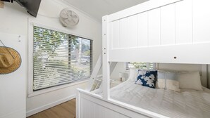 Un lit superposé avec une tête de lit, une fenêtre avec des stores, un ventilateur fixé au mur et un panier en osier.