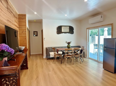 A modern kitchen with wooden cabinetry, a dining area with a table and chairs, a built-in oven, and a large window.
