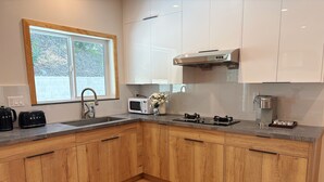 A modern kitchen with wooden cabinets, a built-in microwave, a coffee maker, and a window with a view of trees.