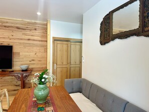 A room with a wooden wall, a television, a wooden table with a vase, a grey sofa, and a door.