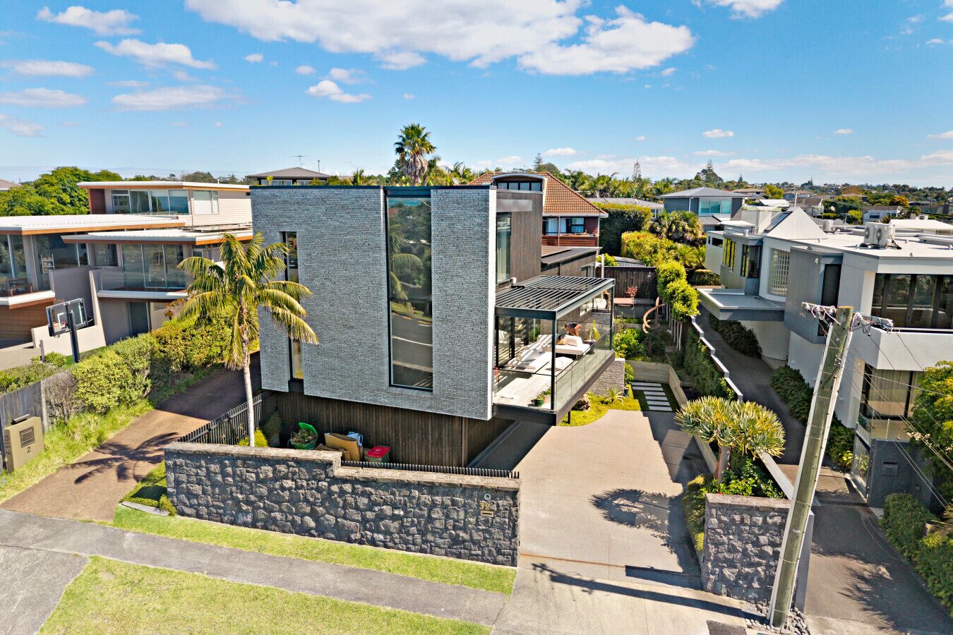 Un moderno edificio residencial con fachada de piedra, un balcón con mobiliario exterior y un jardín cuidado.