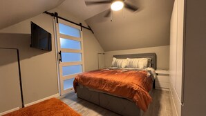 A bedroom with a bed, a ceiling fan, a TV mounted on the wall, and a sliding door. - A Little Country w/ A Little Beach (BOLIVIA)