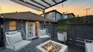 A deck with outdoor seating, a fire pit, and a covered area with string lights. - Brooks Avenue by Avantstay Walk to Venice Beach + Boardwalk Firepit Terrace + EV Charger (Venice)