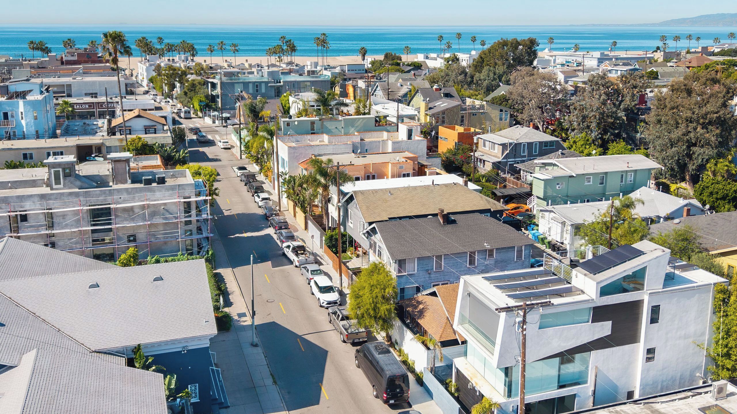 A coastal residential area with modern houses, a street, and a beach in the background.