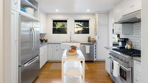 A modern kitchen with white cabinetry, stainless steel appliances, and a central island with fruit. - Brooks Avenue by Avantstay Walk to Venice Beach + Boardwalk Firepit Terrace + EV Charger (Venice)