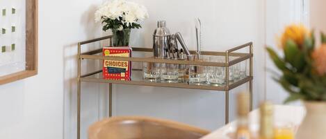 A bar cart with a boxed set of cocktail recipes, a vase of flowers, and various bar tools.