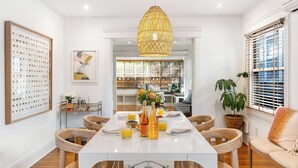 A modern dining area with a white table, wooden chairs, a hanging light fixture, and a view into the adjacent living space. - Brooks Avenue by Avantstay Walk to Venice Beach + Boardwalk Firepit Terrace + EV Charger (Venice)
