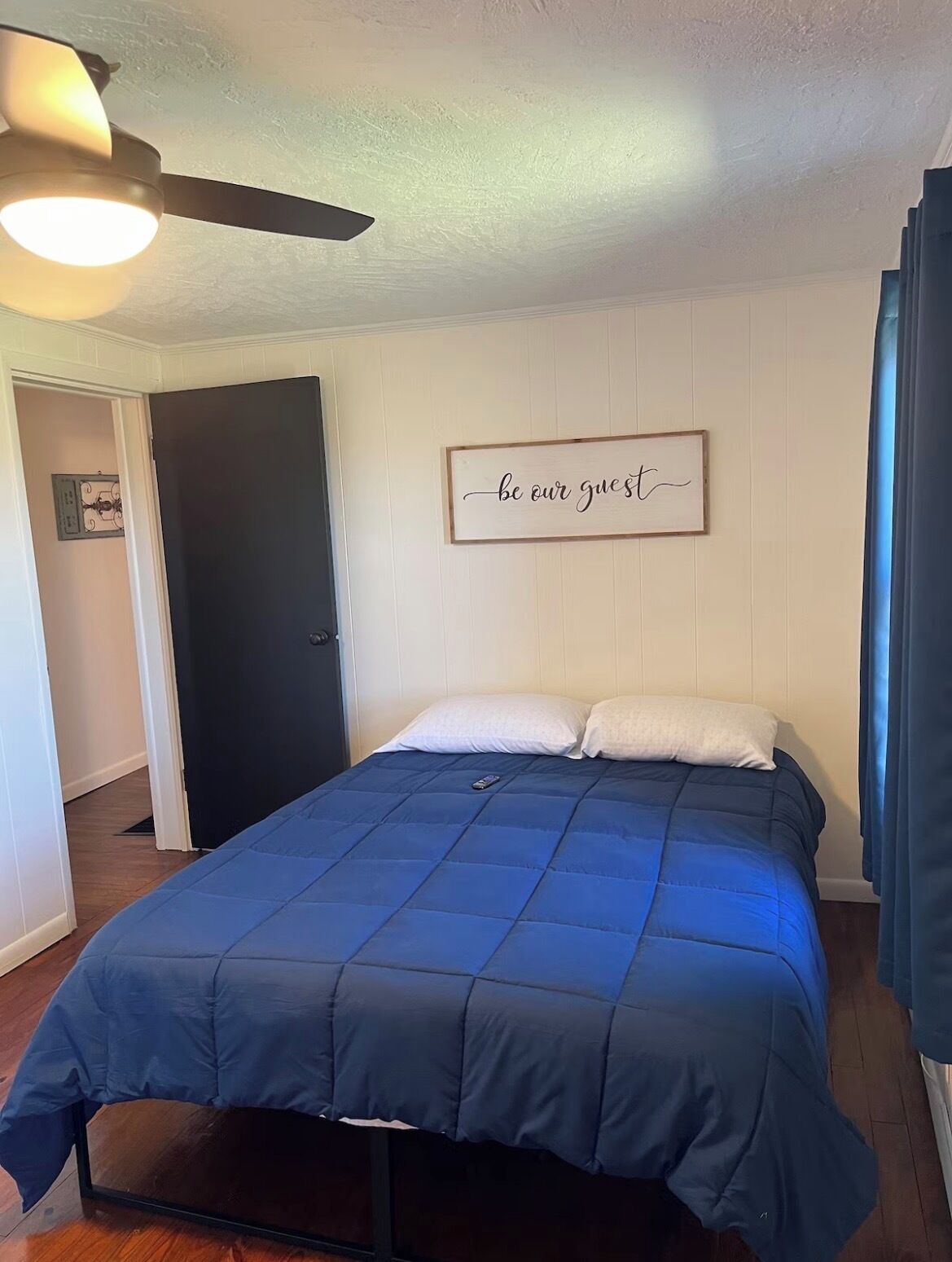 A bedroom with a bed, a ceiling fan, a door, and a wall sign.
