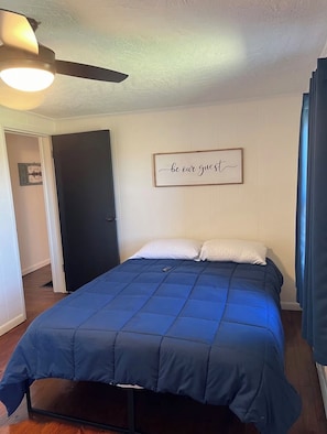 A bedroom with a bed, a ceiling fan, a door, and a wall sign. - Peace & Quiet! 2 Bedroom 1 Bath tucked in the middle of 236 Acres ! AC / WiFi! (Cardington)