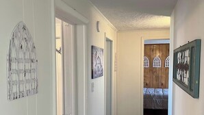 Un pasillo que conduce a un dormitorio con suelo de madera, paredes blancas y una cama con colcha gris.