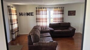 Un salón con dos sofás de cuero marrón, suelo de madera, un letrero con la palabra 'HOME' en la pared y cortinas a rayas.