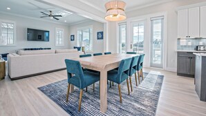 Una cocina moderna con una isla integrada, un comedor con mesa de madera y sillas azules, y un amplio ventanal que proporciona luz natural.
