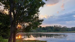 A tranquil lakeside scene with a tree, calm water, and a sunset. - Ama Eco Lodge (WPRH+9G Sigiriya)