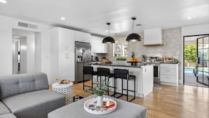 Una cocina moderna con una isla central, taburetes de bar y una zona de comedor con un sofá gris y una pequeña mesita auxiliar.